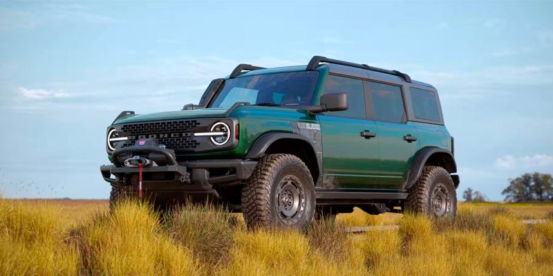 A green 2024 Ford Bronco parked on grassy terrain with clear blue skies in the background
